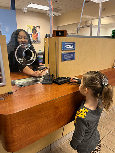SAFE Credit Union Senior Member Service Representative Elexus Alexander teaches preschooler Ryelle Nebeker how to use a signature pad.